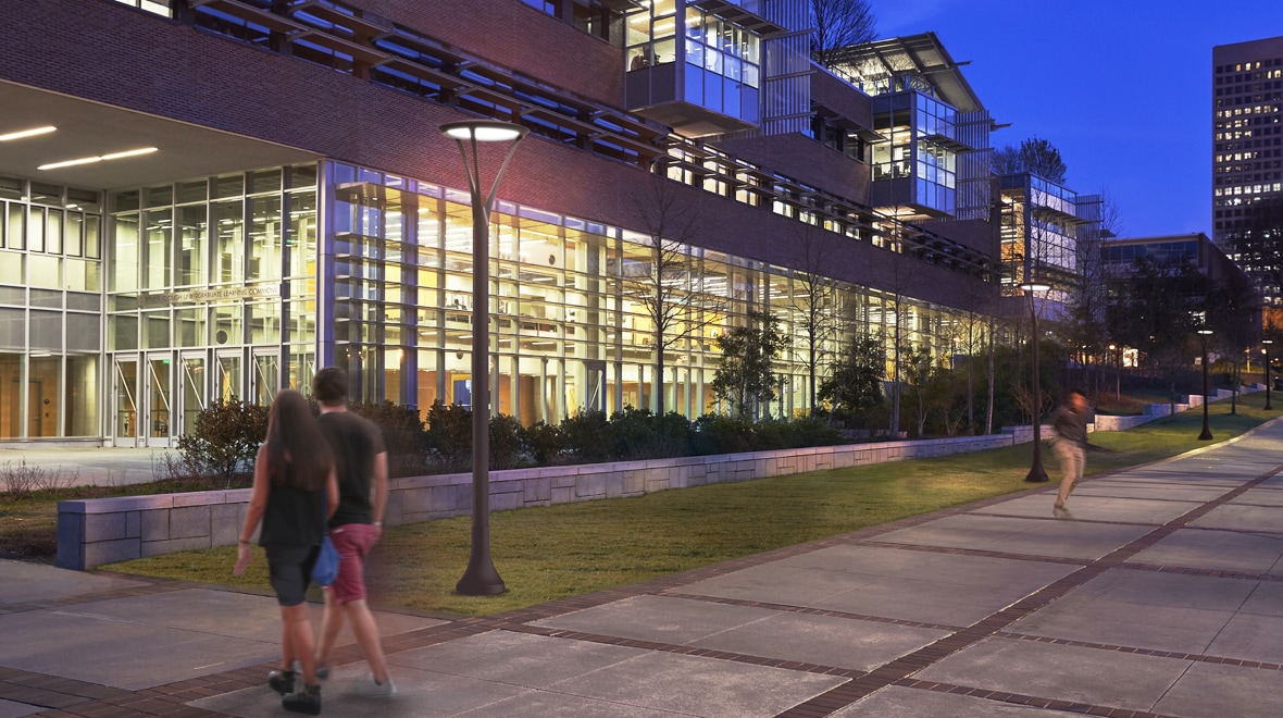 Nighttime- The Luxescape post top luminaire lights up the sidewalk as a college aged skateboarder zooms by.